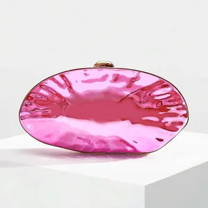 Detail of fuchsia shell clutch bag showing fluid texture and golden sphere lock