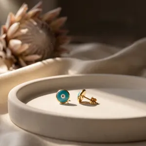 Detail of 18K gold plated evil eye stud earrings with blue enamel on a ceramic plate