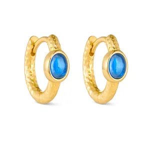 Textured hammered gold hoop earrings with inset round blue zircon gemstone on white background