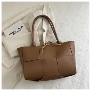 Détail d'un grand sac cabas en cuir tressé marron avec motif damier posé sur un blazer