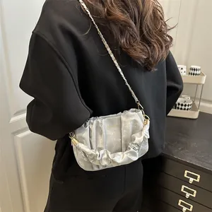 Silver-grey pleated cloud bag with golden chain strap worn by a model in a modern room
