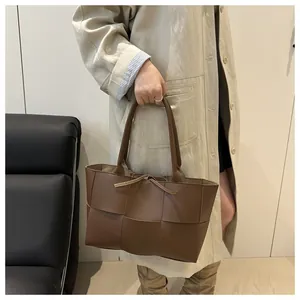 Sac fourre-tout en cuir tressé marron porté par un mannequin en trench-coat beige