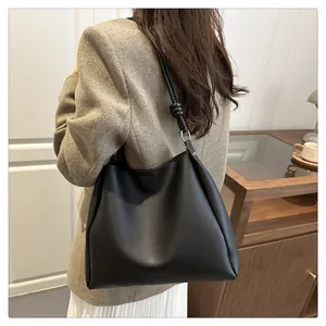 Detail of a black leather tote bag featuring a knotted shoulder strap and silver metal ring