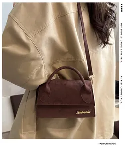 Detail of a dark brown suede crossbody bag with top handle and gold metal logo