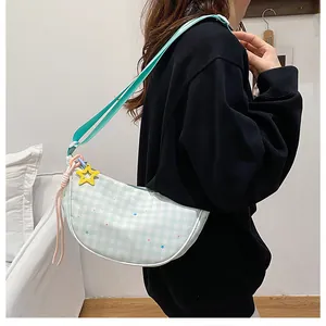 Detailed side view of green plaid half-moon crossbody bag with star charms on a model