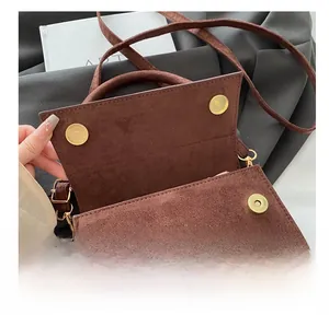 Detail of brown suede shoulder bag featuring gold magnetic buckles and metallic logo