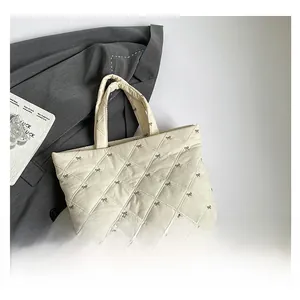 Detail der cremefarbenen Stepptasche mit brauner Schleifenstickerei und Rautenmuster