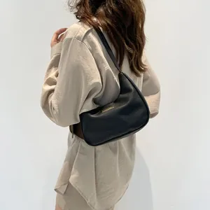 Black pebbled leather underarm bag with gold metal plaque shown on shoulder