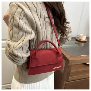 Close-up of red suede crossbody bag with gold logo on white knit sweater outfit