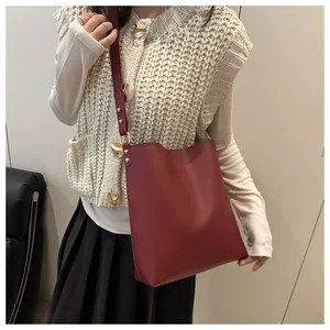 Gros plan du sac seau bordeaux en cuir foulonné avec rivets dorés et bandoulière réglable