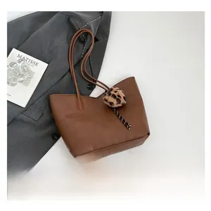 Close-up of brown pebbled leather tote bag with leopard print plush charm and thin straps