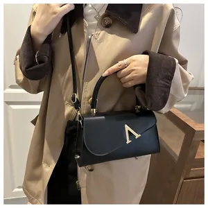 Detail of black leather handbag with golden V-shaped metal buckle and slim shoulder strap