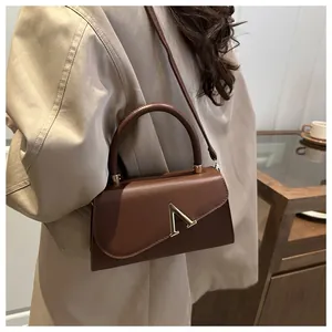 Close-up of brown leather bag featuring an asymmetrical flap and gold V-shaped metal clasp
