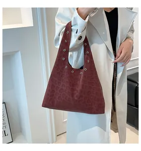 Detail of burgundy leopard print tote bag with metal eyelets on model wearing beige coat