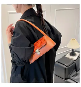Close-up of vibrant orange baguette bag with crocodile texture and silver twist lock