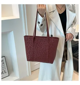 Close-up of a burgundy leopard print tote bag styled with a white coat in a modern setting