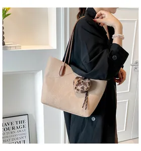 Close-up of beige lychee texture tote bag with brown straps and leopard plush charm
