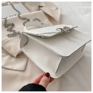 Detail of white PU leather mini bag with silver bow ornament and chain strap