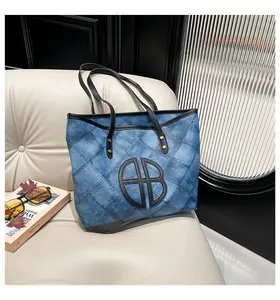 Detail of blue denim patchwork tote bag with black leather straps on a modern leather sofa