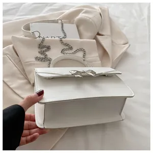 Close-up of a white leather crossbody bag with a silver bow and metallic chain strap
