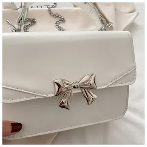 Close-up of a white leather crossbody bag featuring a shiny silver metal bow detail