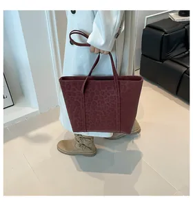 Close-up of burgundy tote bag with subtle leopard print and long handles on a model