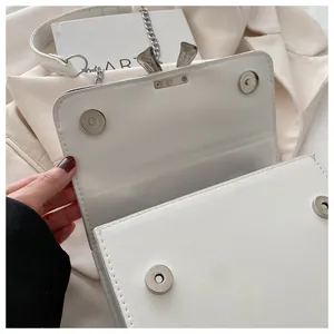 Detail view of white leather crossbody bag showing dual magnetic snap closure and silver hardware