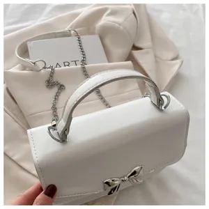 Detail of white PU leather crossbody bag with metal bow decoration and silver chain strap