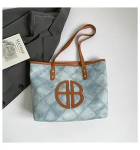 Detail of blue denim tote bag with brown leather handles and circular logo cutout decoration