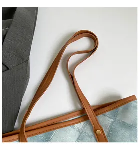 Detail of light blue twill tote with brown leather handles and golden rivet accents