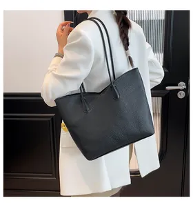 Detail of black pebbled leather tote bag featuring elegant V-shaped stitching on white suit