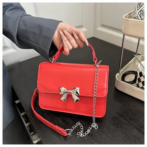 Detail of red leather crossbody bag with silver bow ornament and metallic chain strap