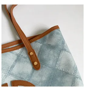 Close-up of blue denim tote bag with brown leather trim and golden metal rivet detail