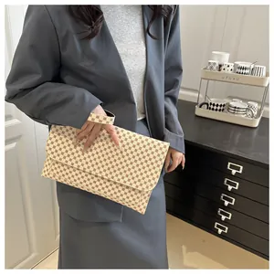 Détail d'une pochette beige vintage à motifs géométriques tenue par une femme en tailleur