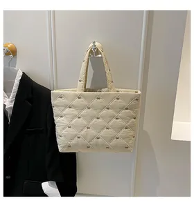 Detail der beige gesteppten Tragetasche mit dunkler Bogenstickerei und Rautenmuster-Textur