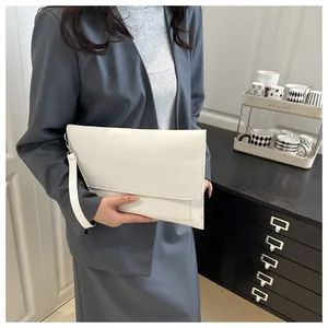 Gros plan d'une pochette enveloppe en cuir blanc tenue par un mannequin en costume gris