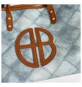 Close-up of quilted denim tote bag featuring brown leather logo and gold metal rivets