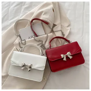 Detail of elegant white and red leather crossbody bags with silver bow and chain straps