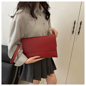 Gros plan d'une pochette enveloppe rouge en cuir mat élégant avec une dragonne assortie