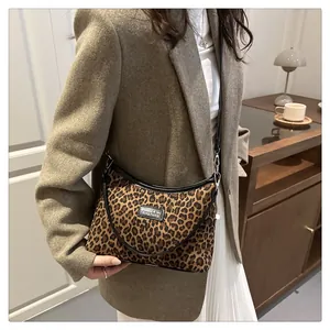 Detail einer Schultertasche mit Leopardenmuster, schwarzem Riemen und quadratischem Logo