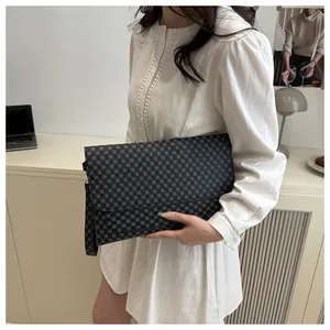 Gros plan d'un sac à main gris foncé à motifs géométriques tenu par un mannequin en robe blanche