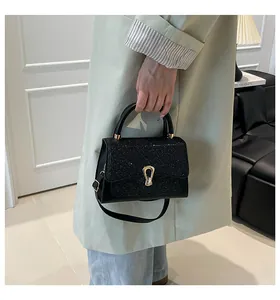 Close-up of black glitter square handbag with gold handle and metallic buckle detail