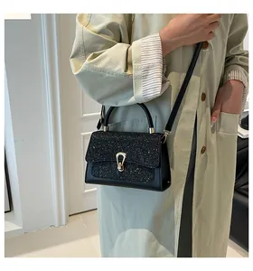 Detail of black square bag with shimmering rhinestones and gold hardware on green trench coat