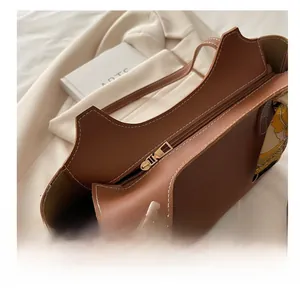 Detail of brown leather tote bag showing smooth metal zipper and silk scarf accessory