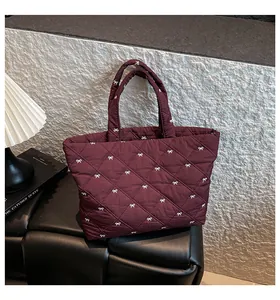 Nahaufnahme der weinroten Stepp-Tasche mit weißen Schleifenstickereien und Rautenmuster