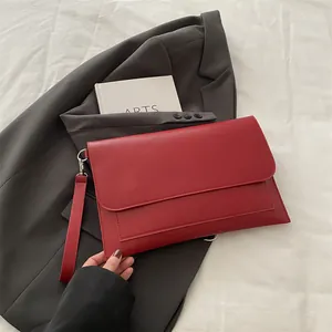 Détail d'une pochette enveloppe rouge en similicuir lisse avec dragonne métallique amovible