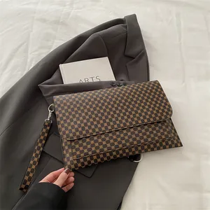 Détail d'une pochette enveloppe marron avec monogramme portée avec un blazer gris chic