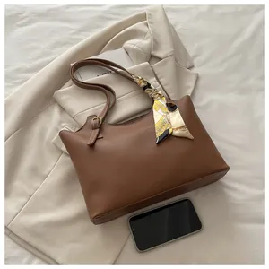 Detail of a brown leather tote bag with a floral silk scarf and metal strap buckle