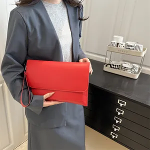 Pochette enveloppe élégante en cuir rouge avec dragonne, tenue par un mannequin en costume