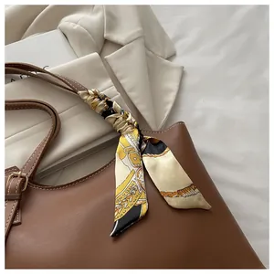 Detail of a brown leather tote bag with a patterned silk scarf on the handle